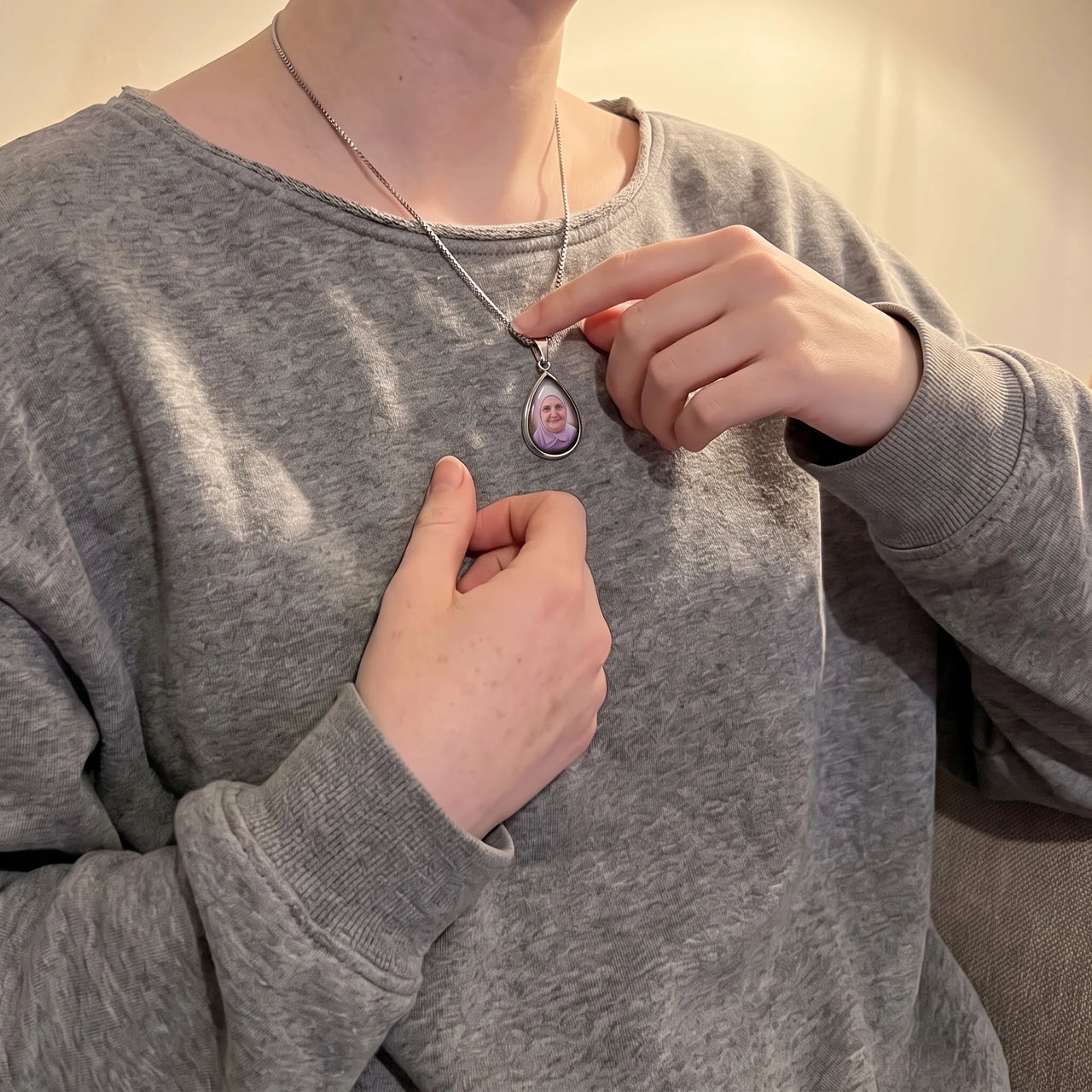 Woman in a grey sweatshirt touching the silver teardrop pendant to reveal the photo | SKU: TPH-DRPN-SILVER