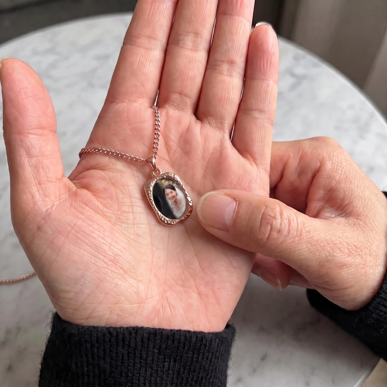 Thumb warming the rose gold oval pendant: the hidden photo appears under the thumb while the rest stays black | SKU: TPH-OVLN-ROSEGOLD
